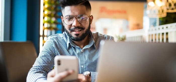 Un hombre interactuando con un teléfono móvil y una laptop